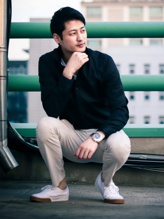 Stylish Asian man in casual attire poses on a rooftop with cityscape backdrop in Seoul.